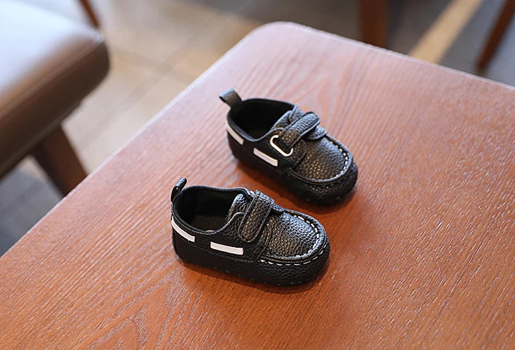 Two black children's shoes with velcro straps on a wooden surface.