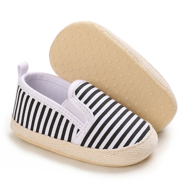 Black and white striped baby shoes with beige soles on a white background
