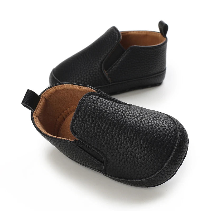 Pair of black baby shoes with brown soles on a white background