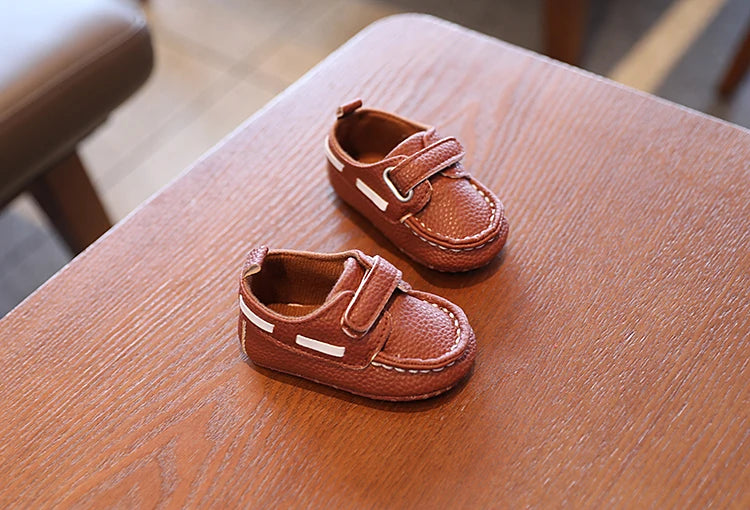 Pair of brown children's shoes with velcro straps on a wooden surface