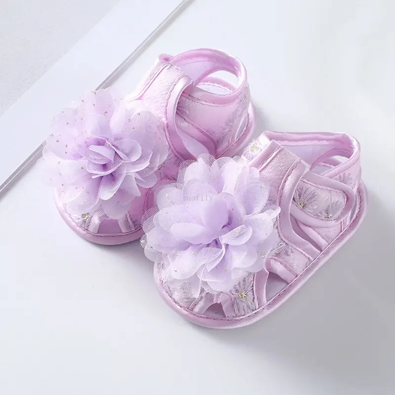 Pair of purple baby sandals with floral decorations on a white background