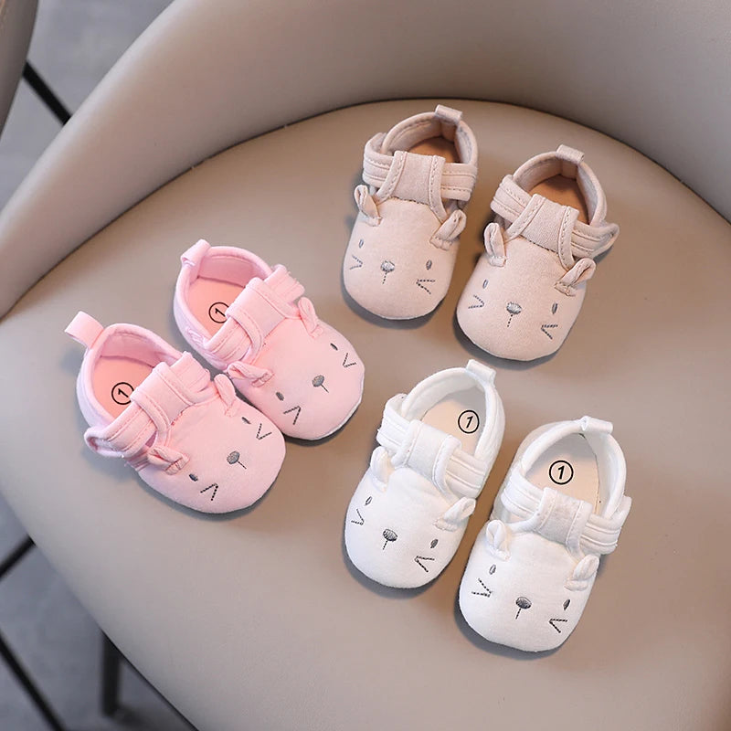 Set of pink and white baby shoes with cartoon designs on a beige surface.