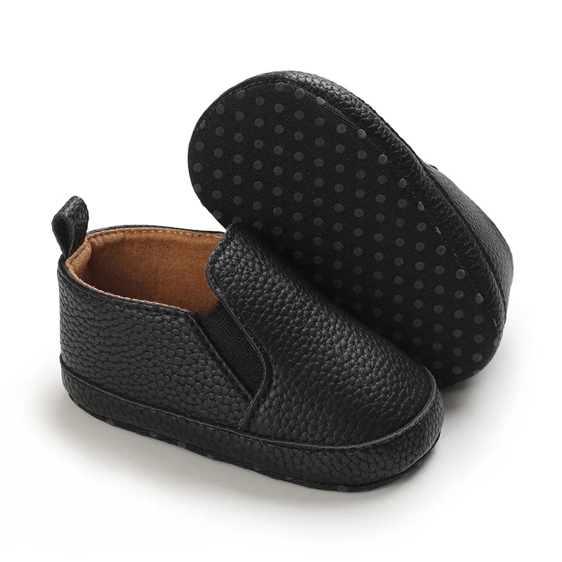 Black baby shoes with textured sole on a white background